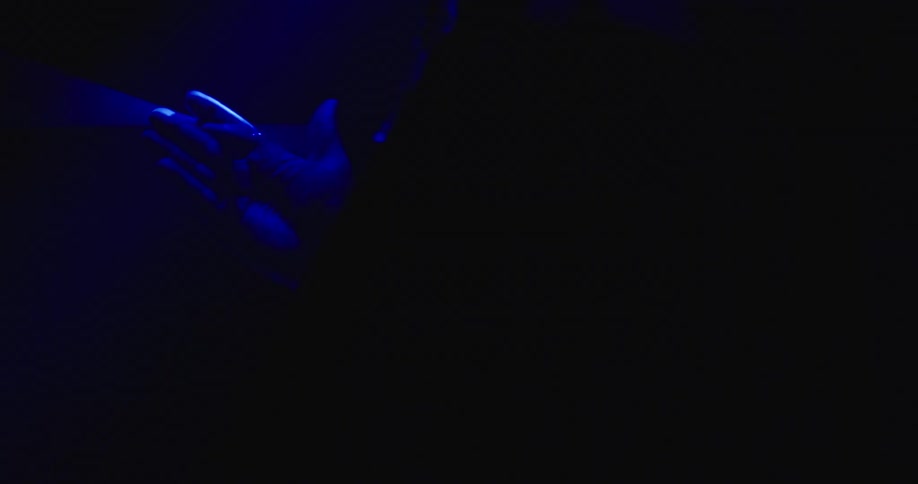 A person with a hat twirling drumsticks in a room with blue lights