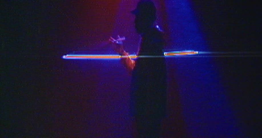 A musician stands on a stage with bright lights and twirls a drumstick in his hand