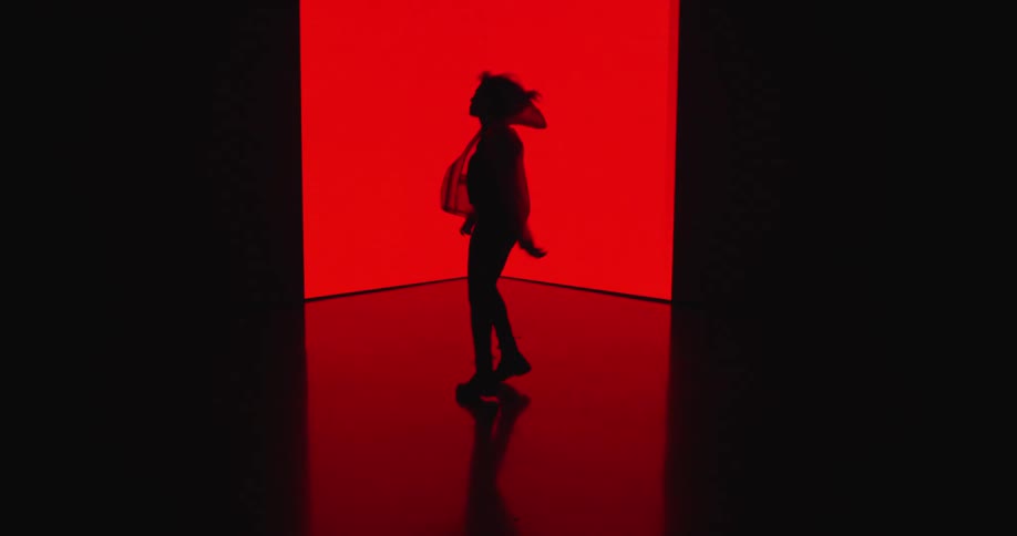 A silhouette of a woman with a jacket dancing in a room with a wall in the background