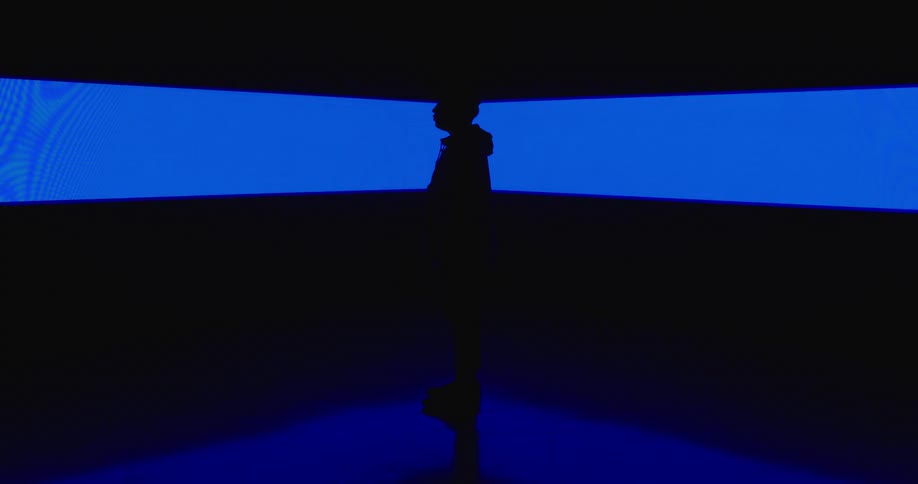 A silhouetted man standing in front of a glowing blue wall