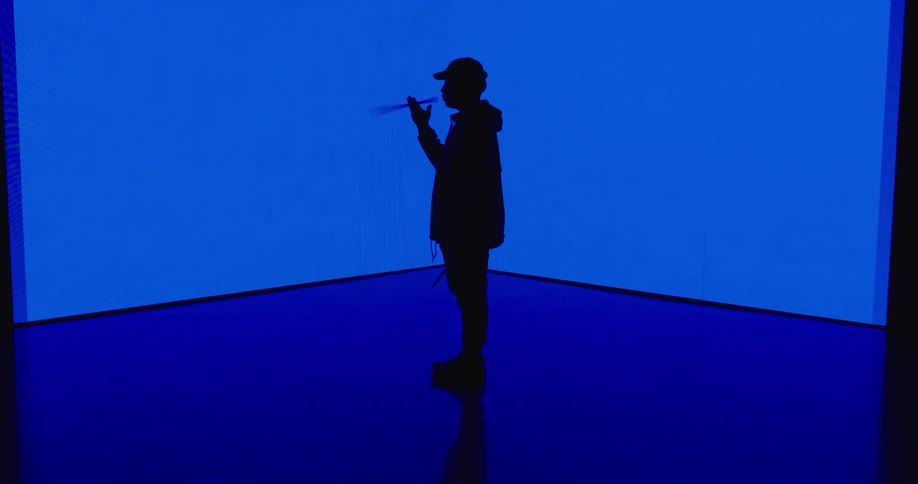 A silhouette of a man spinning a drumstick in a room with blue lights