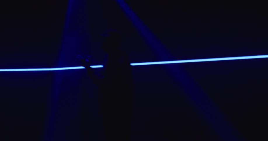 A man with a hat twirling a drumstick in a room with a screen in the background