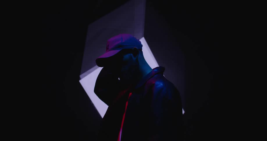 A man adjusting his baseball cap while standing in front of a rotating digital cube