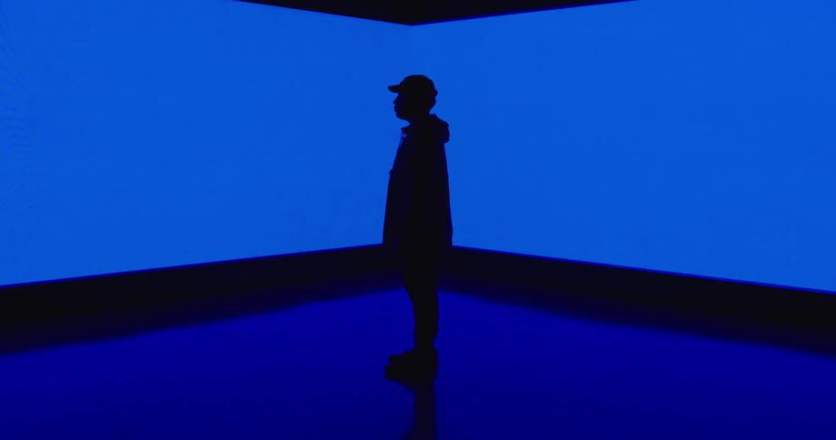 The silhouette of a man is seen as he stands in front of a large digital screen that has color wipe across it