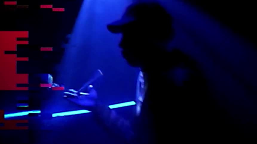 A drummer stands on stage and twirls drum sticks in his hand under color changing spotlights