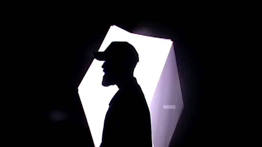 The silhouette of a man in profile with a white cube of light rotating behind him