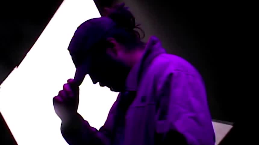 A man with a hat and jacket in a room with a screen in the background