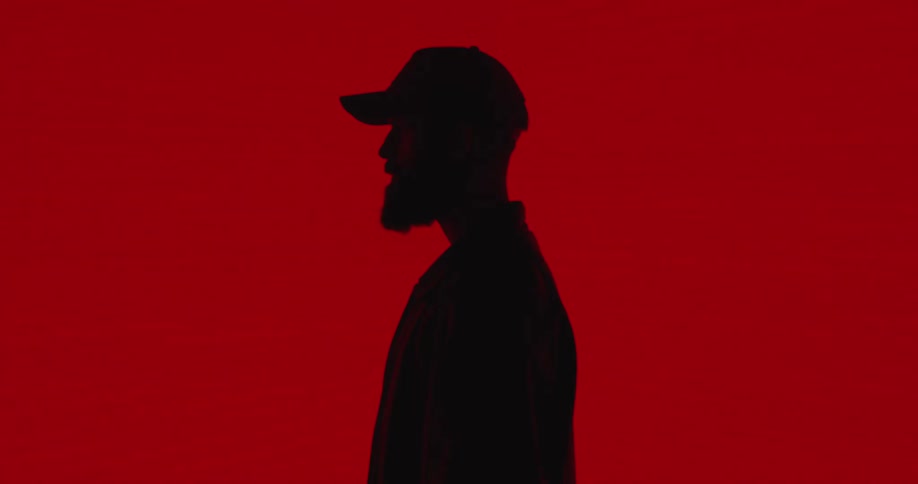A person is posing in the dark with a red wall