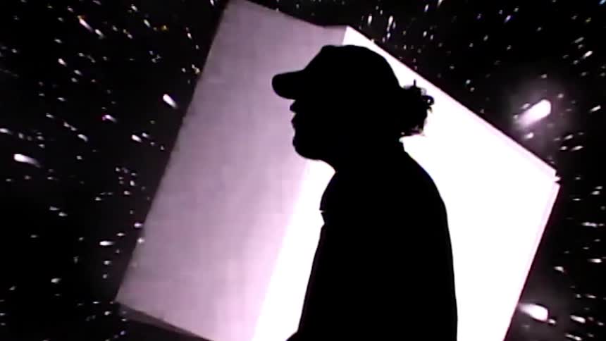 A man stands in front of a large screen with shpaes flashing on them