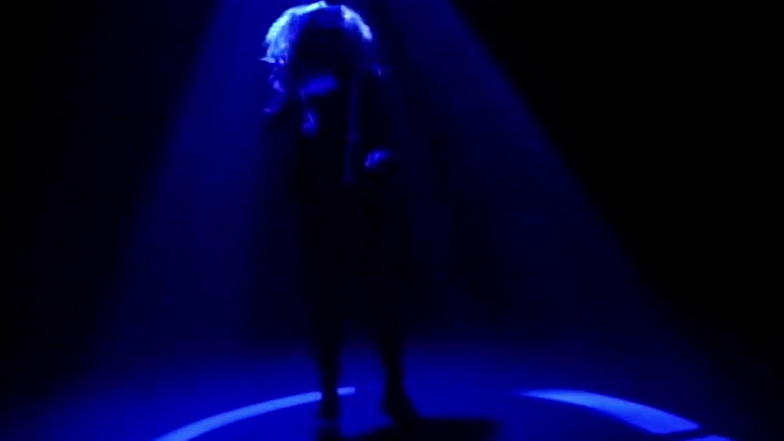 A woman dancing and jumping beneath a spotlight on stage