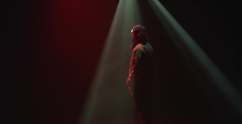 Man standing under the changing coloful lights of a spotlight inside a dark room