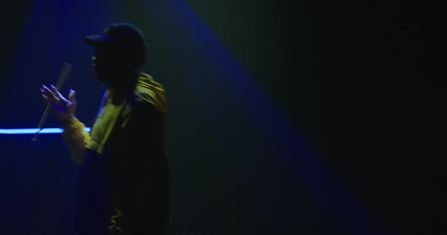 A spotlight shining on a drummer with a drumstick in a dark room