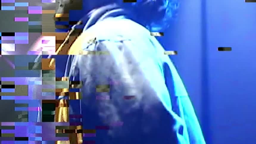 A man stands next to a dark stairwell as the screen turns to static and pixelated colors