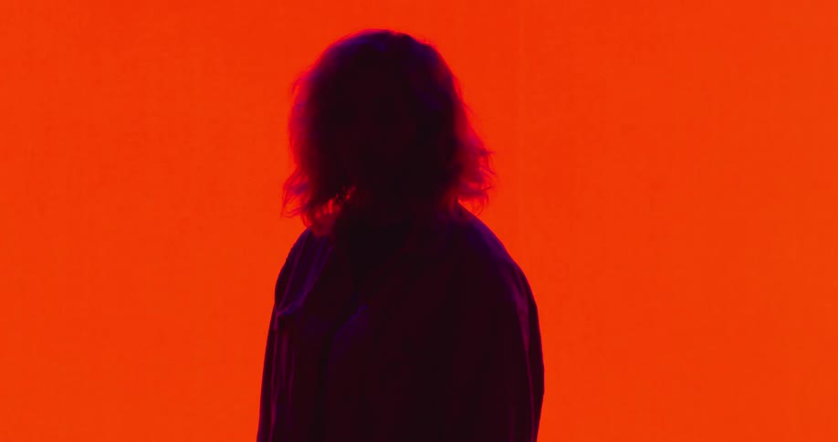 A woman stands in a thick coat in front of a screen that repeatedly changes from red to black