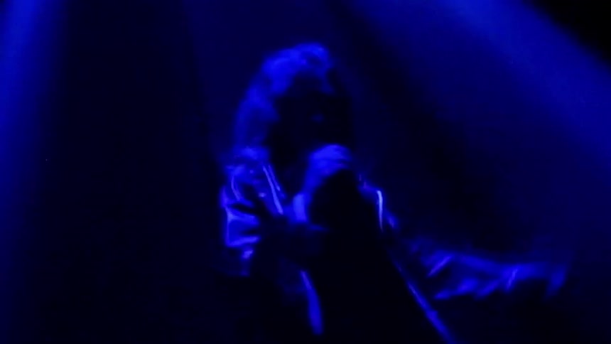 A female dances and twirls around in a dark room beneath a purple light