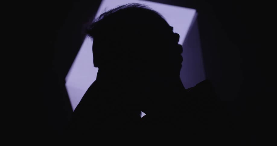 A silhouetted man standing in front of a screen with a rotating digital cube