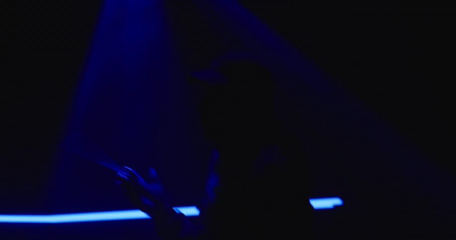 Drummer spinning a drumstick on his fingers under blue lights inside a dark room
