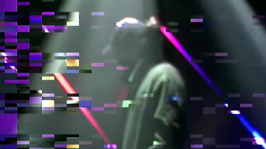 A man with a hat and jacket in a room with laser lights in the background
