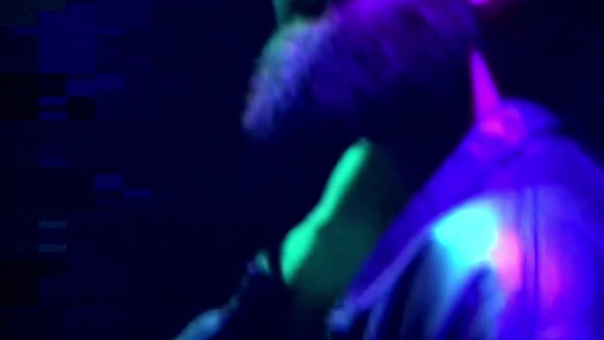 A man adjusts his baseball cap as he stands under color changing neon lights