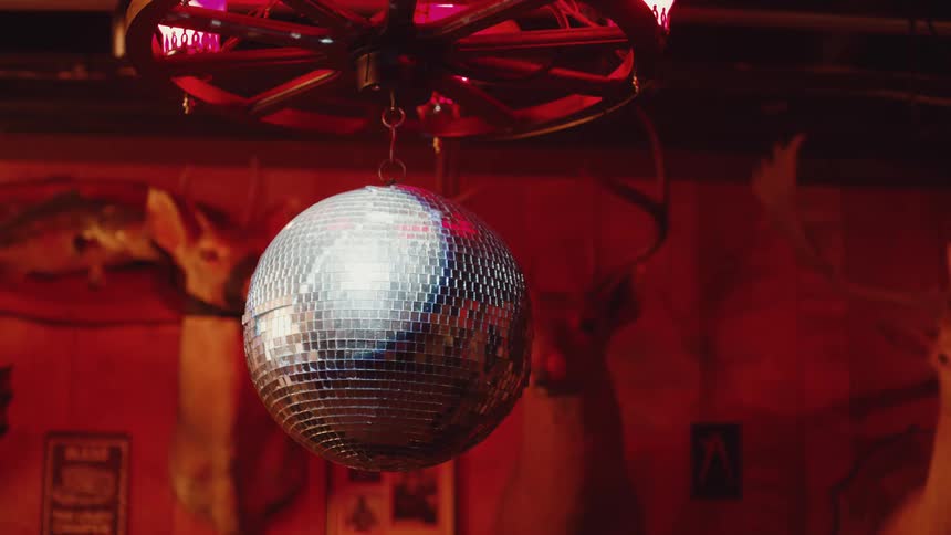 Spinning mirror ball hanging near wall with stuffed animal heads reflects light in red lit club