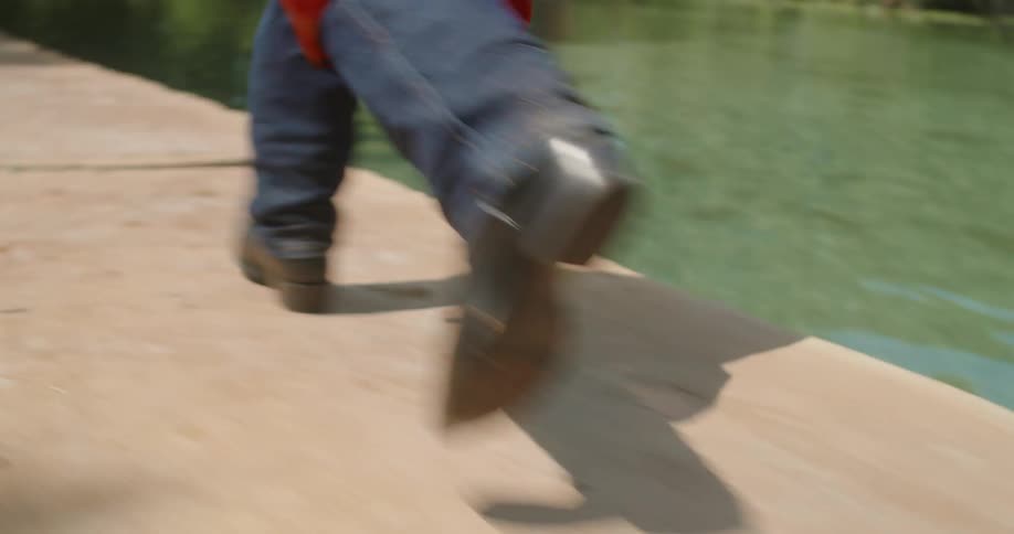 Man wearing a red graduation gown and carrying a grad hat runs and jumps into a river