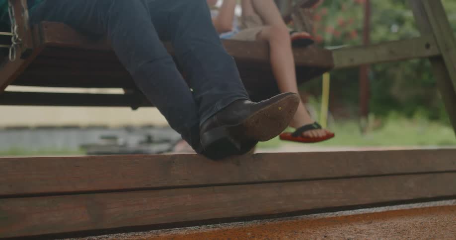 A man and young boy relaxing on a porch swing in the summertime