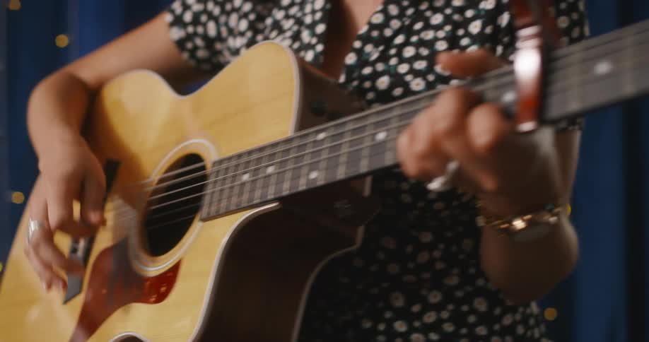 A woman is sitting down and playing an accoustic guitar