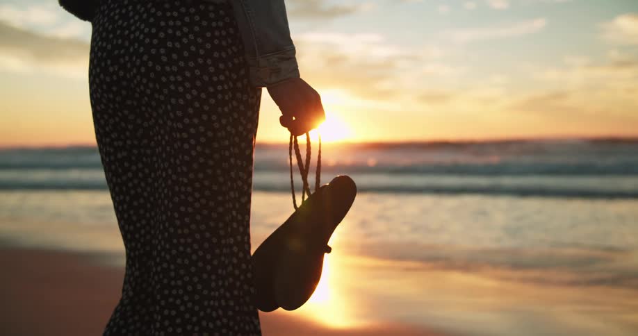 A woman is walking on the beach at sunset