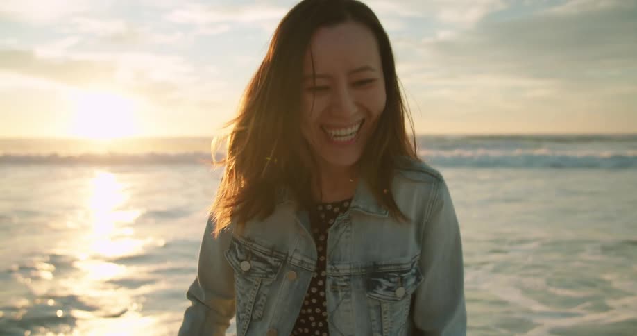 Woman smiles and laughs on beach as sun reflects off ocean waves