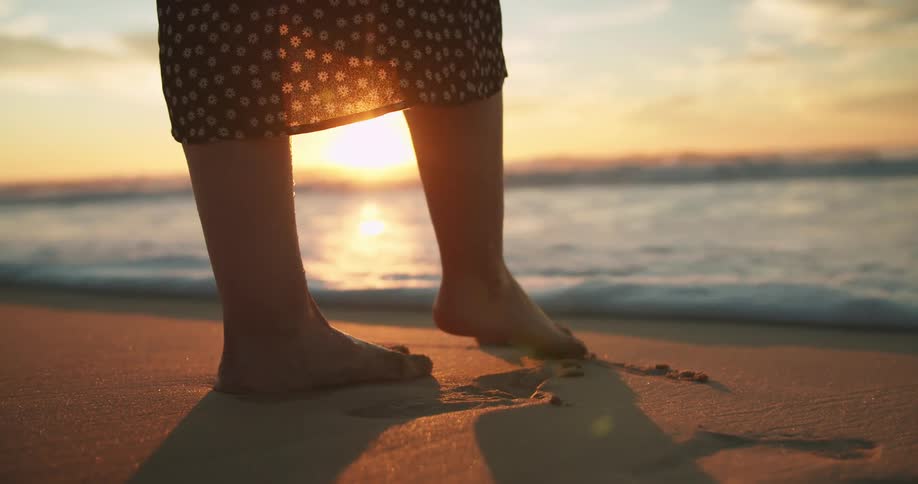 Woman stands on the beach as the ocean water rolls in and covers her feet