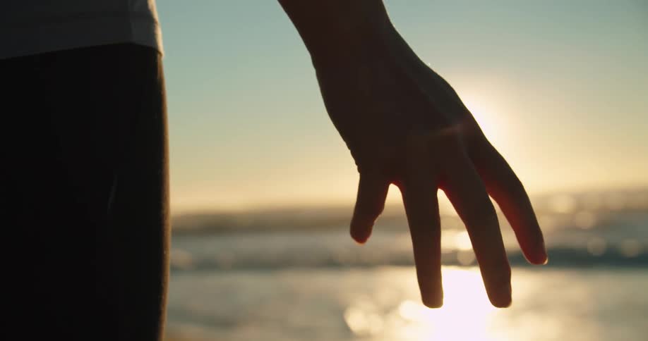 A silhouetted hand backlit by the sun on a beach