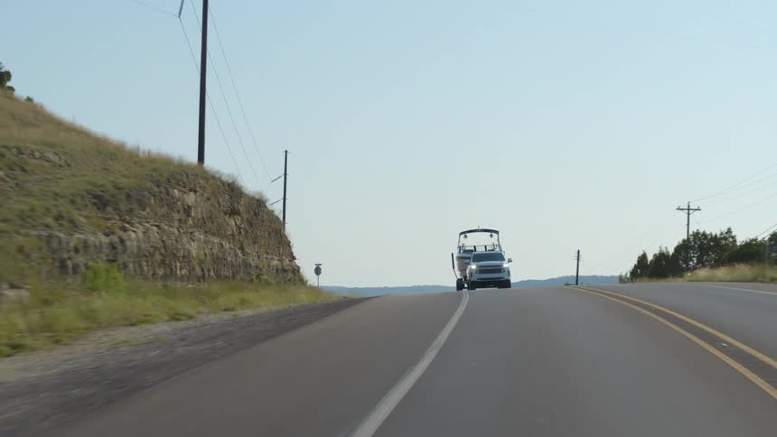 A truck with a boat attached drives along a rural road