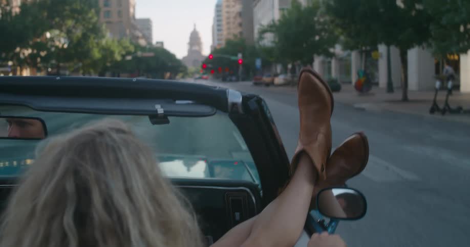Woman with her feet hanging out of the window of a convertible car driving on the city streets