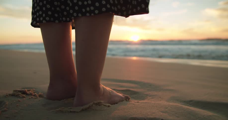 A woman stands on a beach as the sun sets