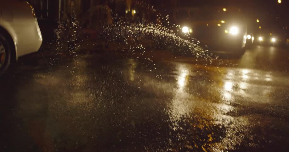 Water sprays out of a fire hydrant onto the city street at night