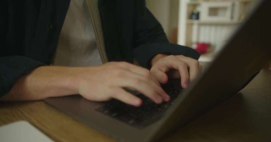 A man is typing on a laptop and sitting indoors