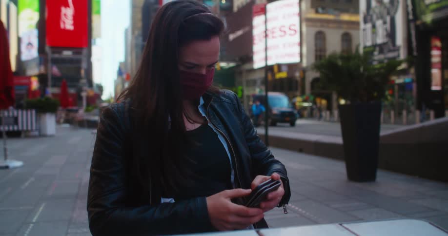 A woman with a mask sitting at a table using a smart phone in times square