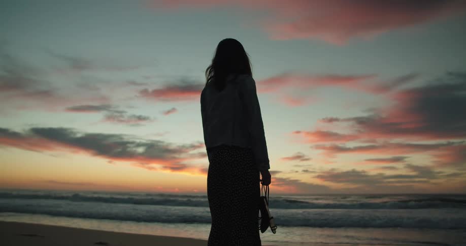 Silhouette of a woman standing in the beach next to the ocean at sunset