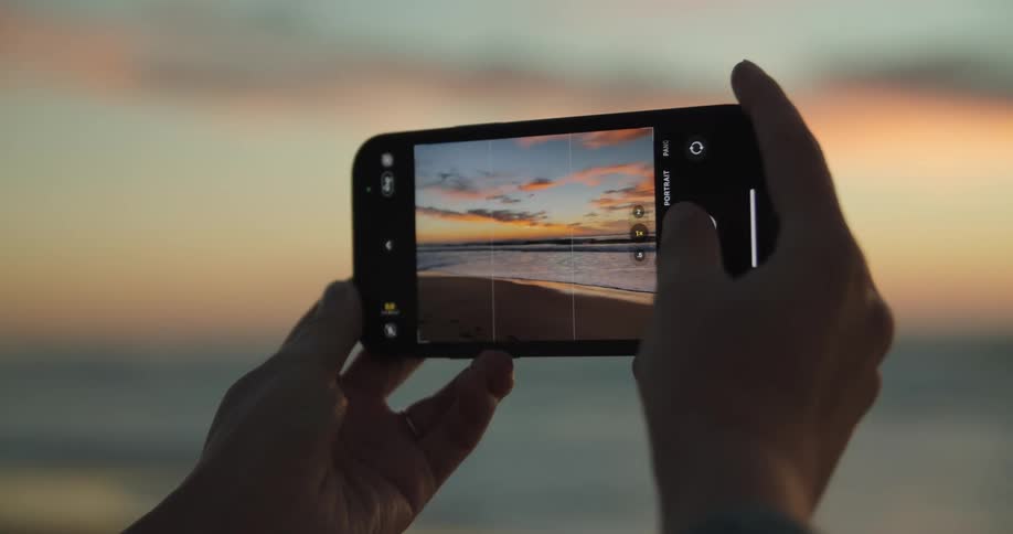 Woman taking pictures of the sunset over the ocean with a smartphone