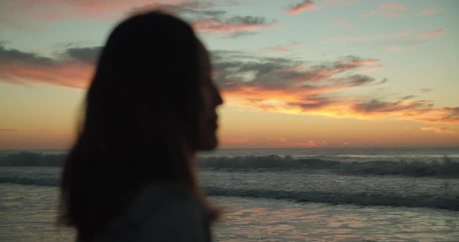 A woman stands on the shore and watches the waves roll in