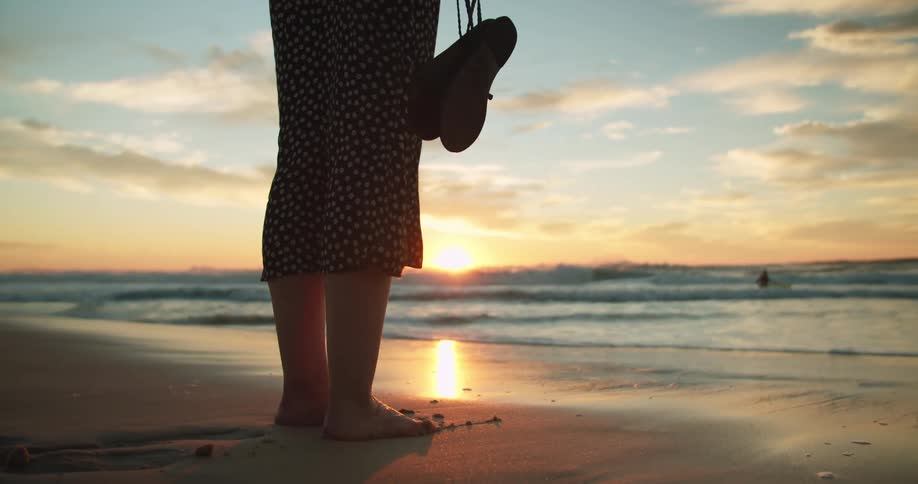 A woman is standing at the coast of a beach at dusk