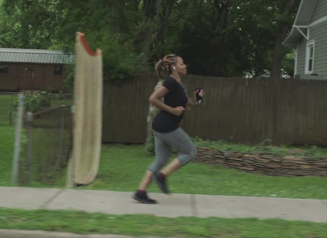 Woman with braids a black t shirt and grey leggings runs along the pavement in the neighborhood