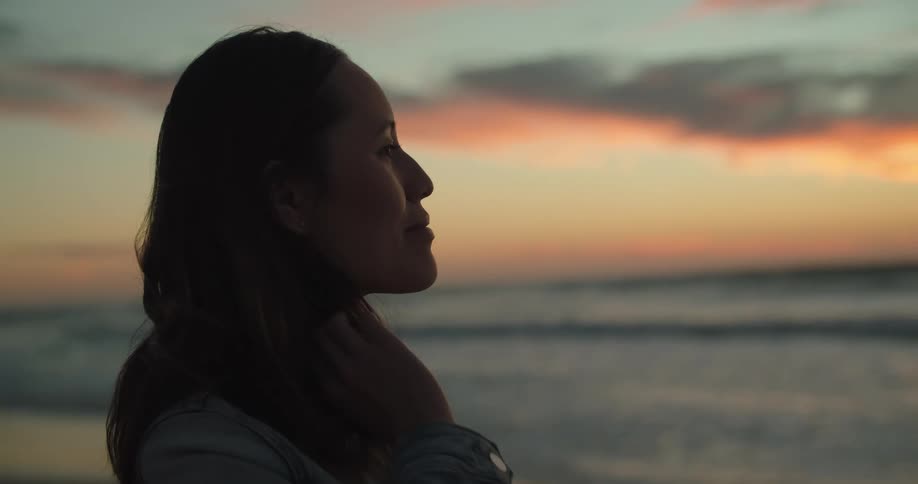A woman is standing outdoors at the beach at dusk