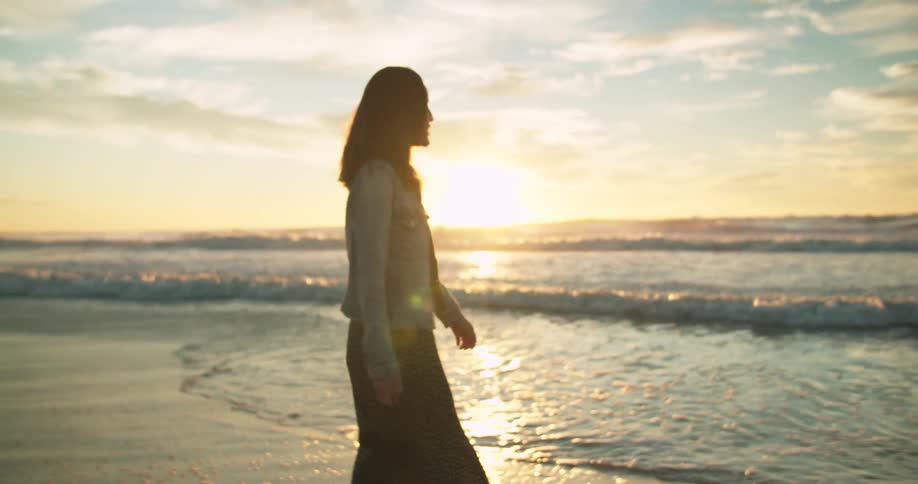 Woman walking on the beach shoreline next to the ocean at sunset