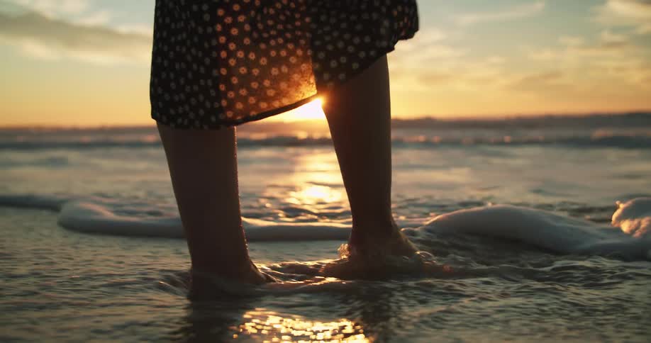 A woman wades in the ocean in a floral sundress