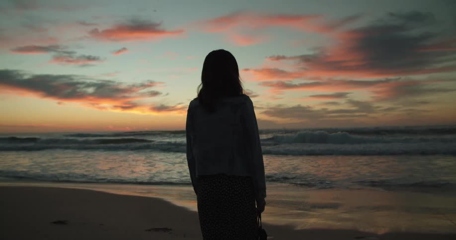 A silhouette of a woman standing on a beach with the sky and clouds in the background