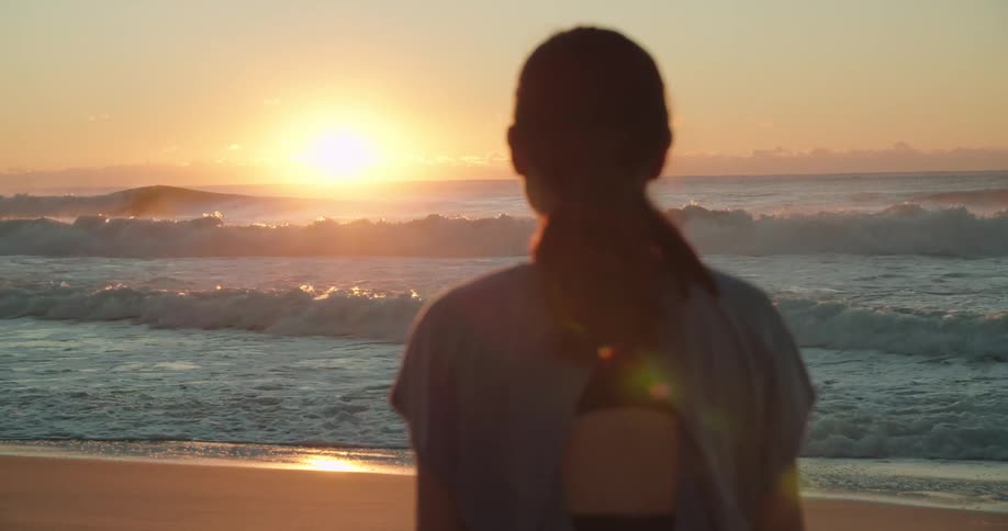 Woman looks out over the rough ocean water as the sun sets