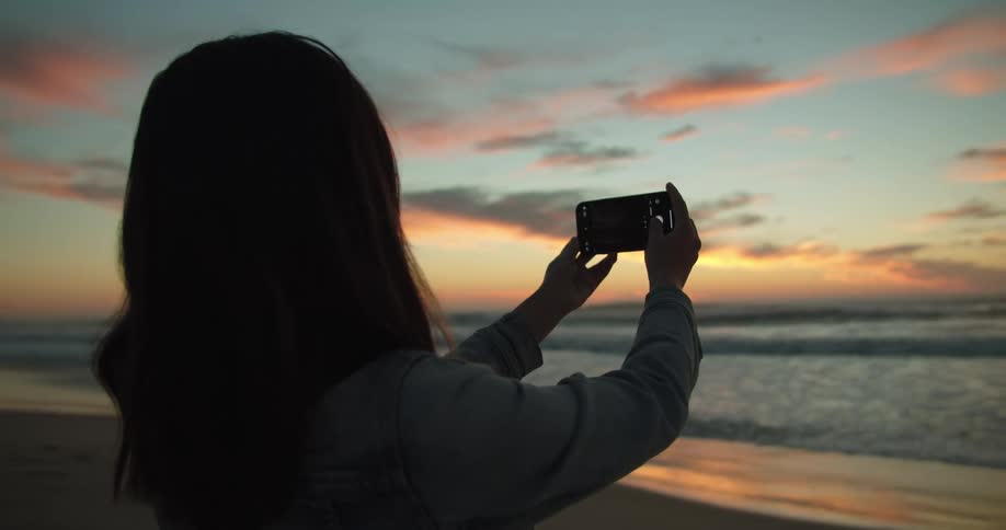 A woman is photographing the beach at sunset