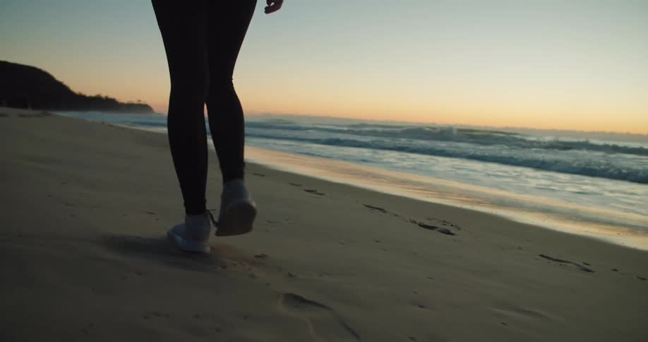 Woman with black leggings and sneakers walks along the beach at dusk