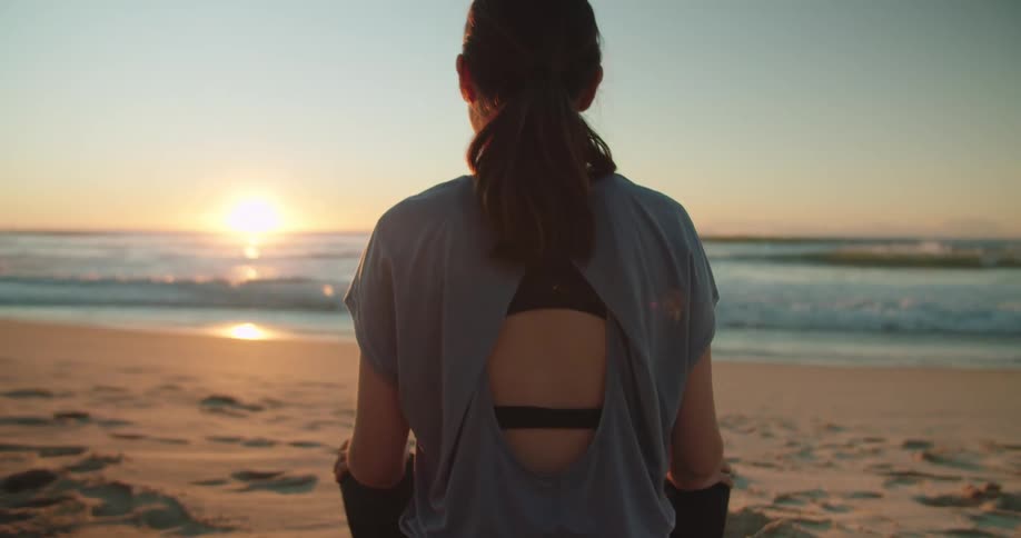 A woman meditating alone on a sandy beach at sunset